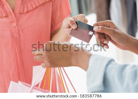 Closeup mid section of female customer receiving shopping bags and credit card from saleswoman in boutique