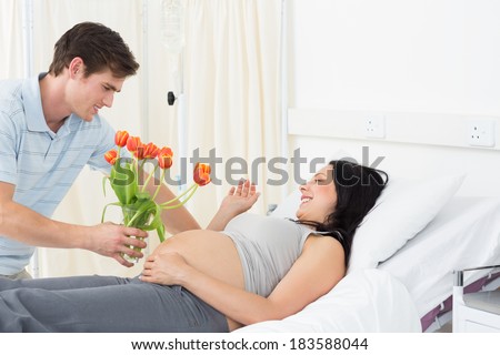 Young man offering flowers to pregnant woman lying in bed in hospital