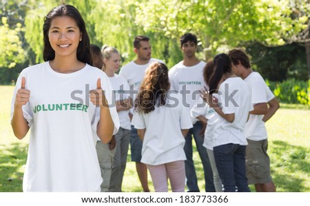 Portrait of confident volunteer gesturing thumbs up at park with friends in backgorund