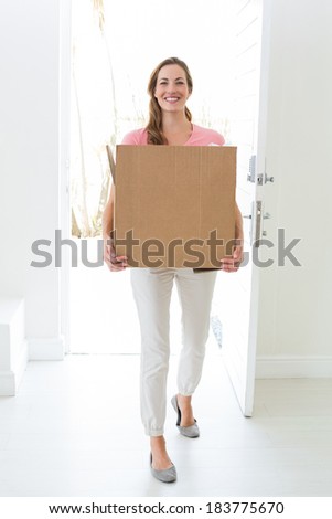 Full length portrait of woman carrying cardboard box in new house