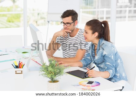 Side view of casual photo editors using graphics tablet in the office