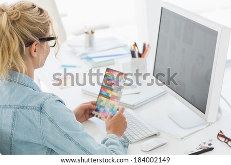 Blonde designer holding colour swatch at her desk in creative office