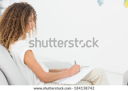 Therapist taking notes on clipboard sitting on couch at therapy session