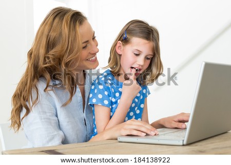 Mother teaching daughter to use laptop at home