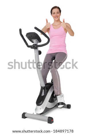 Full length of a beautiful young woman gesturing thumbs up on stationary bike over white background