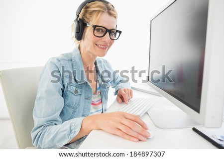 Blonde designer wearing headphones working at computer smiling at camera in creative office