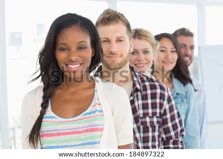 Diverse design team standing in a line smiling at camera in creative office