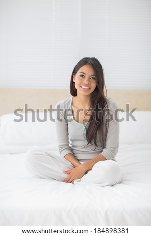 Young girl sitting on bed smiling at camera in her bedroom at home