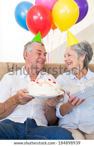Senior couple sitting on couch celebrating a birthday at home in living room