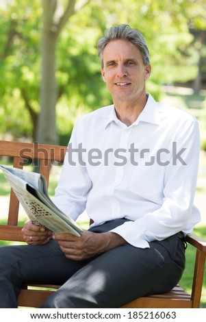 Portrait of happy businessman holding newspaper in the park