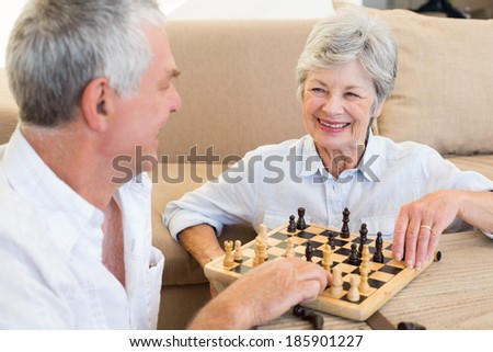 Senior couple sitting on floor playing chess at home in living room