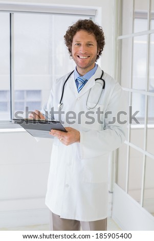 Portrait of a happy handsome male doctor with clipboard standing in the hospital