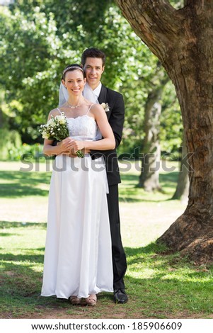 Full length portrait of groom and bride with flower bouquet in park