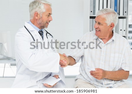 Smiling senior patient and doctor shaking hands in the medical office