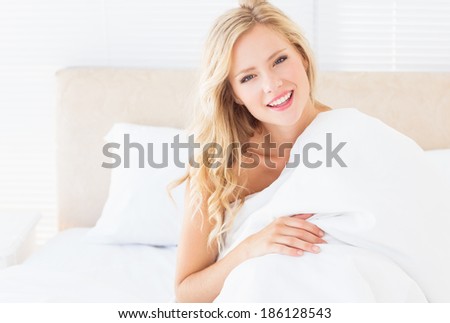 Attractive young woman covering herself with duvet at home in the bedroom