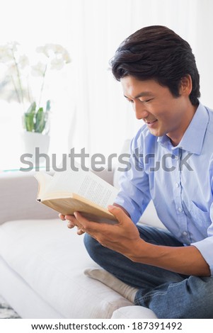 Happy man sitting on couch reading at home in the living room