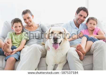 Happy family sitting on couch with their pet labrador at home in the living room