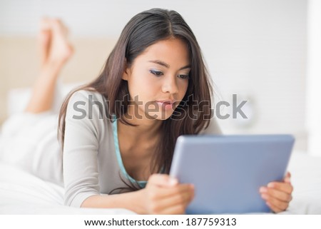Happy girl lying on bed using her tablet pc in her bedroom at home