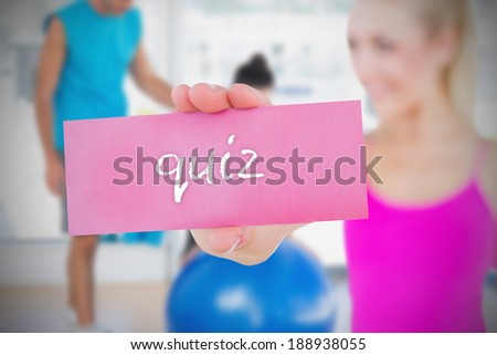 Fit blonde holding card saying quiz against trainer and client in fitness studio
