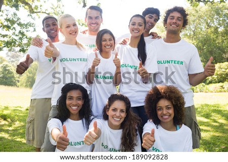 Group portrait of confident volunteers gesturing thumbs up in park