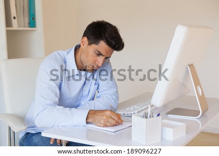Casual businessman writing at his desk in his office
