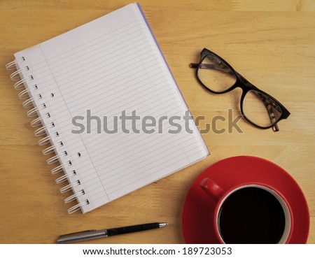 Overhead of notebook and glasses with pen and coffee cup on a desk
