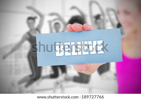 Fit blonde holding card saying believe against dance class in gym