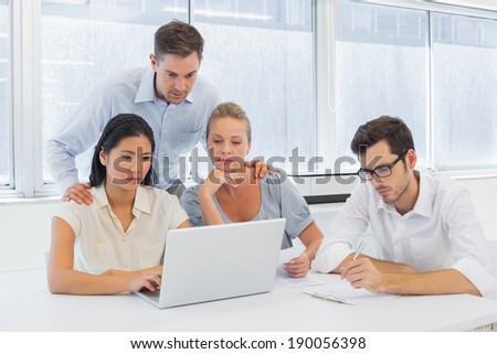 Casual business team working together at desk using laptop in the office