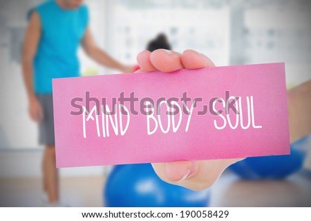 Woman holding pink card saying mind body soul against trainer and client in fitness studio