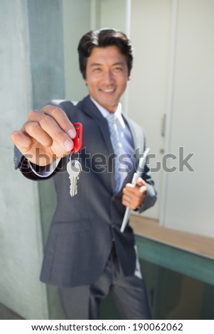 Confident estate agent standing at front door showing key outside a house
