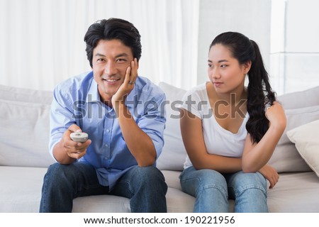 Woman sitting on couch while boyfriend watches tv at home in the living room