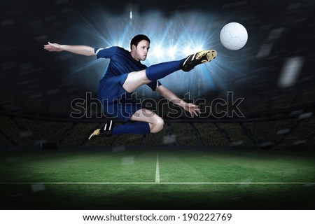 Football player in blue kicking in a football pitch under spotlights