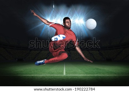 Football player in red kicking in a football pitch under spotlights