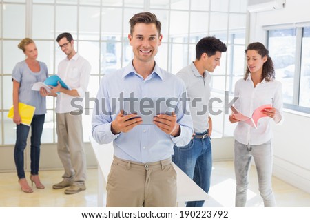Casual boss smiling at camera in front of business team in the office