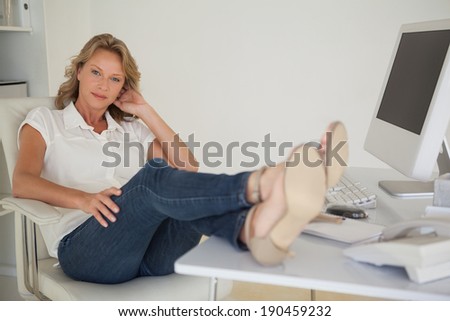 Casual businesswoman sitting at her desk with feet up in her office