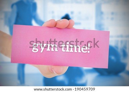 Woman holding pink card saying gym time against trainer and client in fitness studio