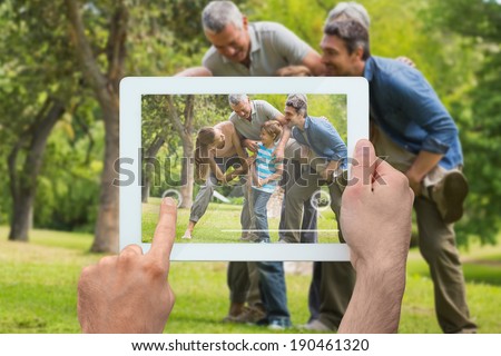 Hand holding tablet pc showing extended family having fun in the park