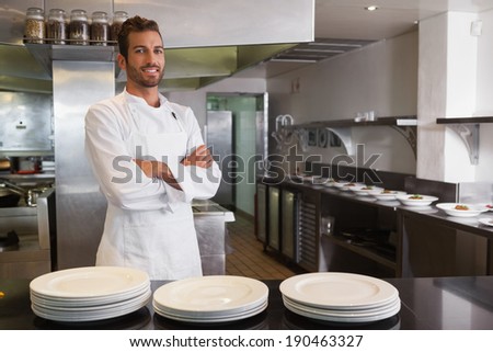 Smiling young chef standing with arms crossed behind counter in a commercial kitchen