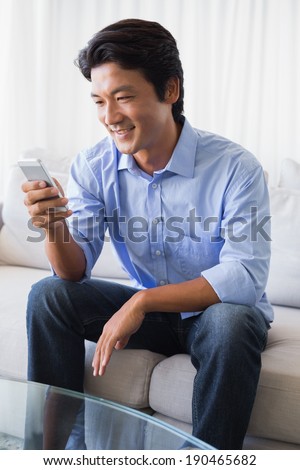 Happy man sitting on couch texting on phone at home in the living room