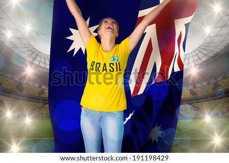 Excited football fan in brasil tshirt holding australia flag against large football stadium with lights