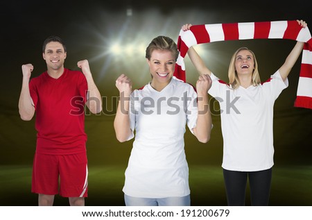 Composite image of various football fans against football pitch under spotlights