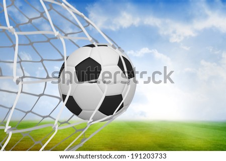 Football at back of net against football pitch under blue sky
