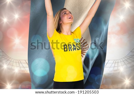 Excited football fan in brasil tshirt holding argentina flag against large football stadium under cloudy blue sky