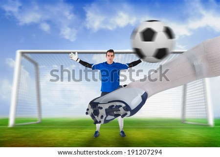 Composite image of football player striking ball at goalkeeper against football pitch and goal under blue sky