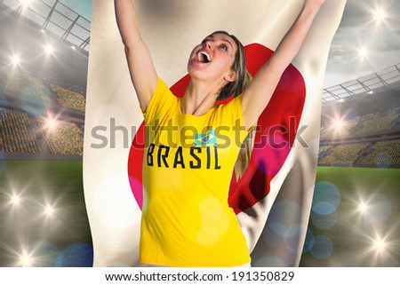 Pretty football fan in brasil t-shirt holding japan flag against large football stadium with lights