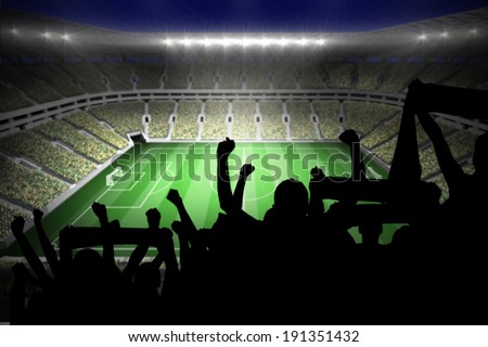 Silhouettes of football supporters against large football stadium with lights