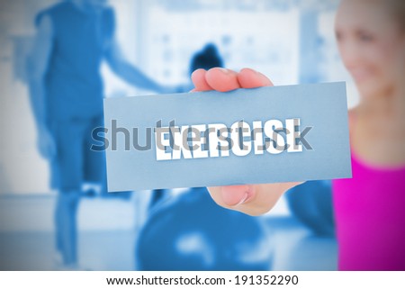 Fit blonde holding card saying exercise against trainer and client in fitness studio