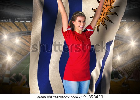 Cheering football fan in red holding uruguay flag against vast football stadium with fans in yellow