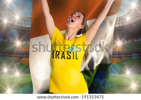 Pretty football fan in brasil t-shirt holding ivory coast flag against large football stadium with brasilian fans
