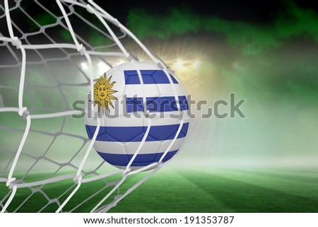 Football in uruguay colours at back of net against football pitch under green sky and spotlights